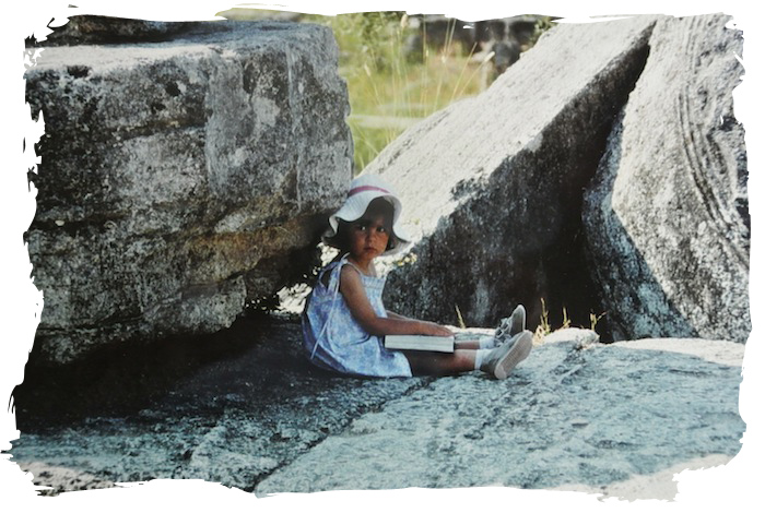©1984, UrbisMedia. A little French girl reads in the shade of a toppled column drum at ancient Olympos, Greece. Is she really wondering whether she should be in the gym working on that balance beam routine?